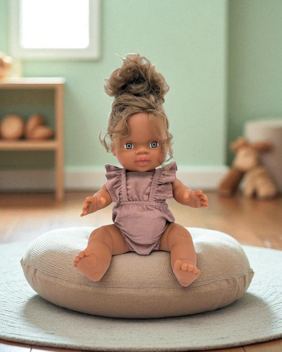 Doll sitting on a cushion in a room with a green wall and wooden floor.
