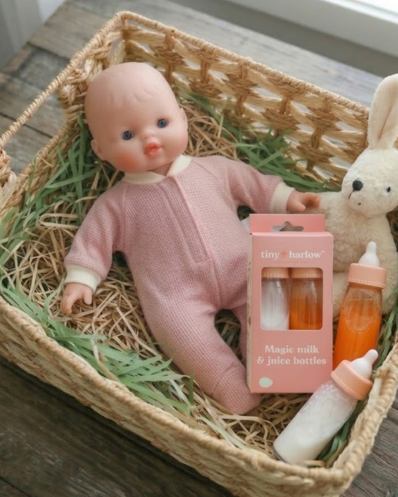Toy doll in a pink outfit with bottles and a rabbit plush toy in a woven basket.
