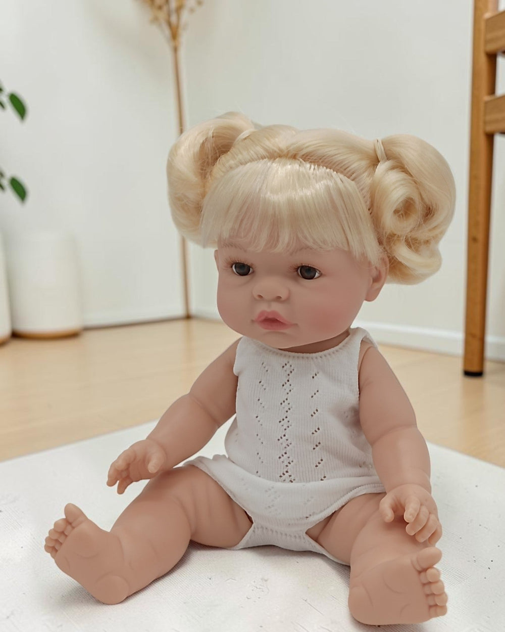 Baby doll with blonde hair styled in pigtails sitting on a white surface.