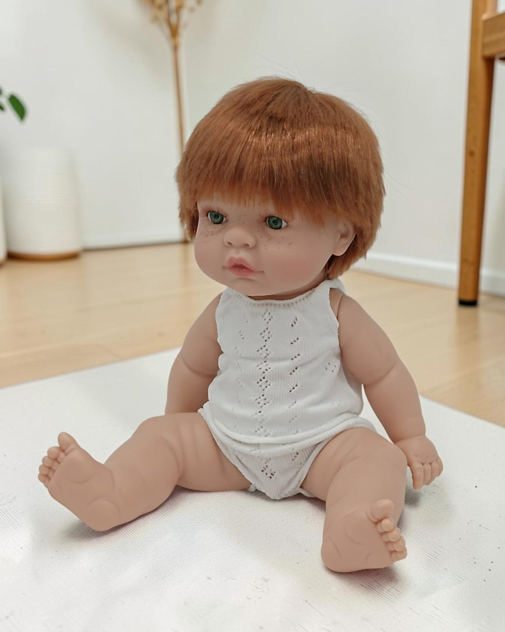 Baby doll with red hair wearing a white outfit on a light surface.