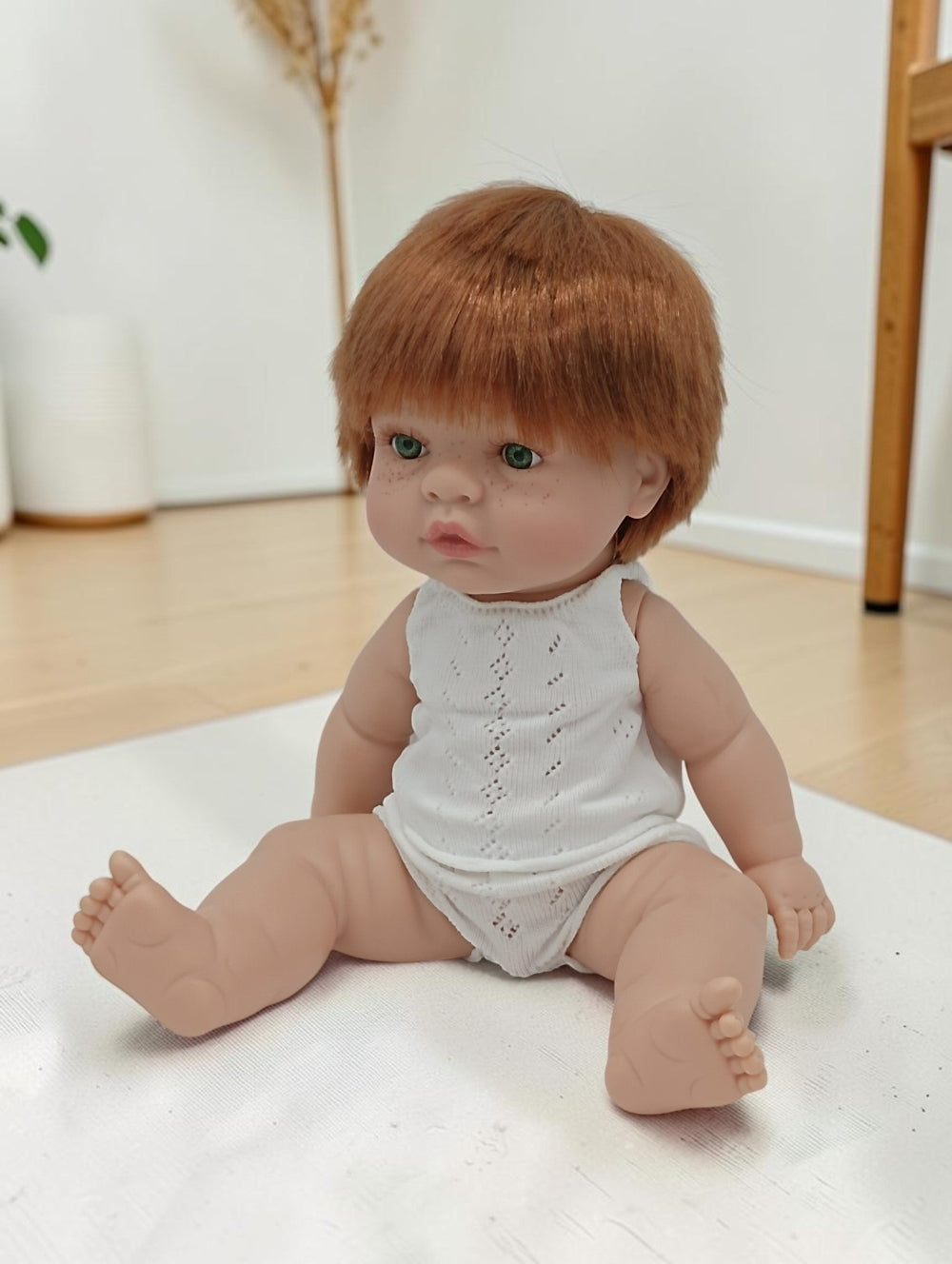 Baby doll with red hair wearing a white outfit on a light surface.