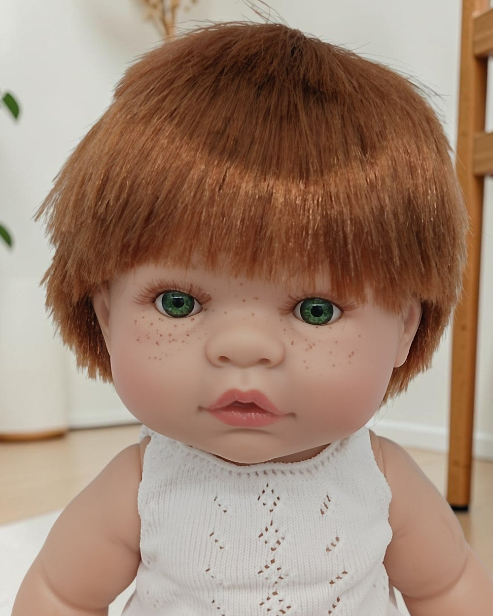 Realistic doll with brown hair and freckles wearing a white sleeveless top.