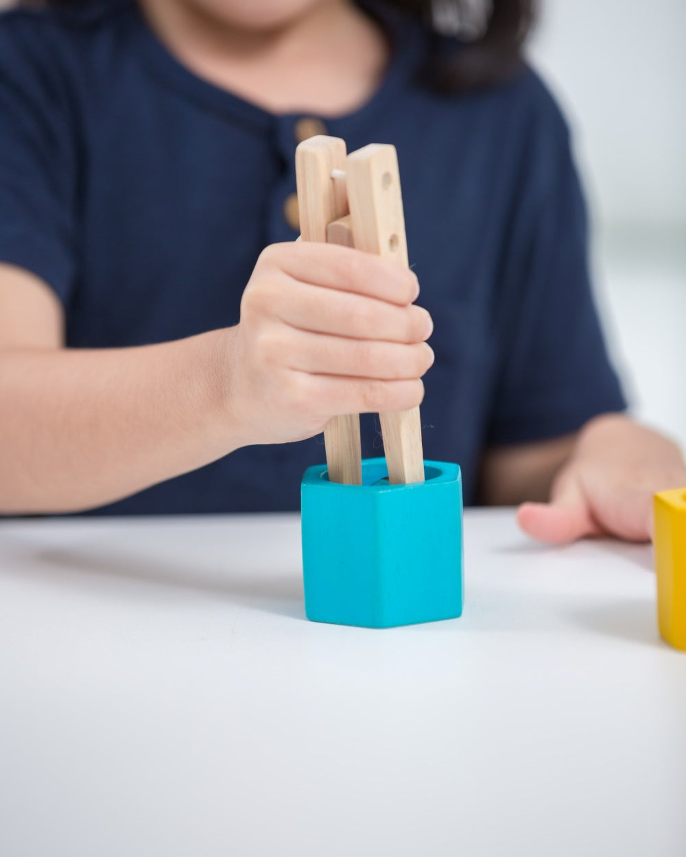 Child using wooden tongs to sort PlanToys colorful bees into hives