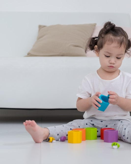 Child playing with colorful blocks on a white floor in front of a white couch.