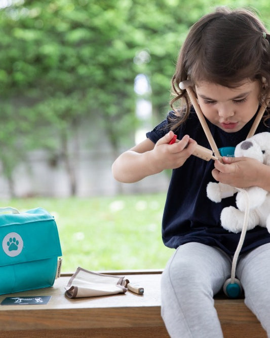 Child playing with a toy in a park, with a teal bag and small pouch on a table.