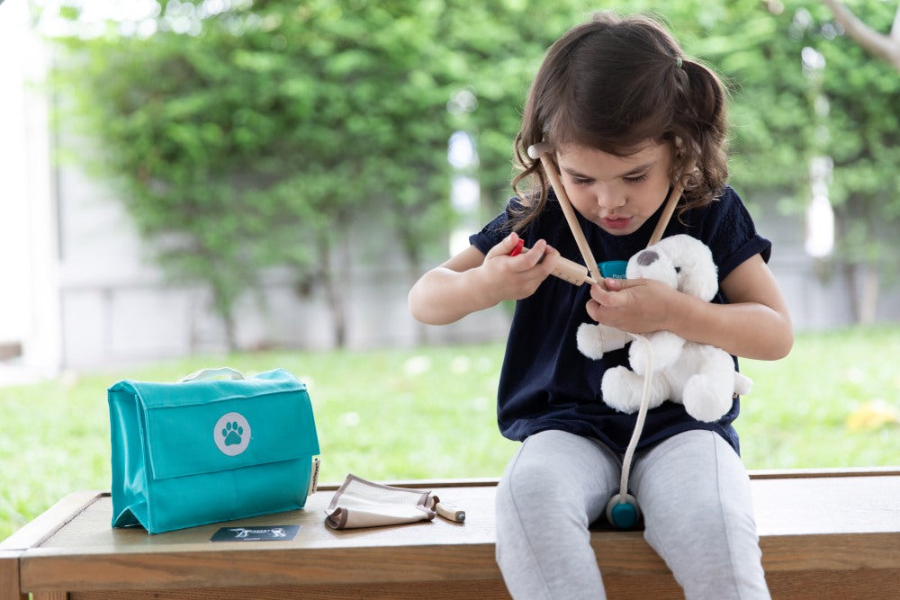 Child playing with a toy in a park, with a teal bag and small pouch on a table.