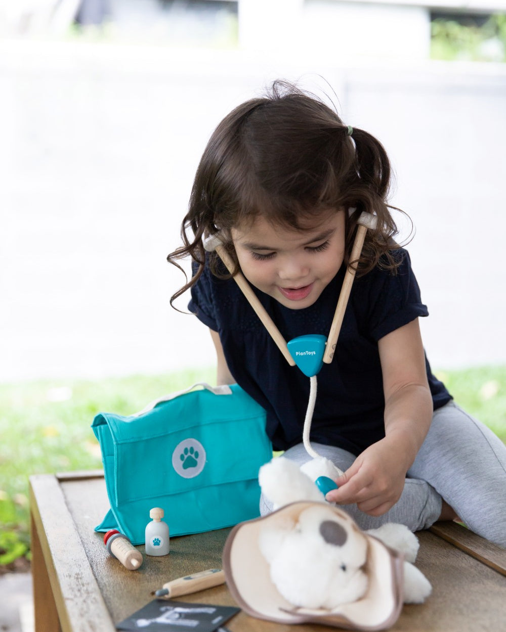 Child playing with a toy doctor set on a wooden table outdoors.