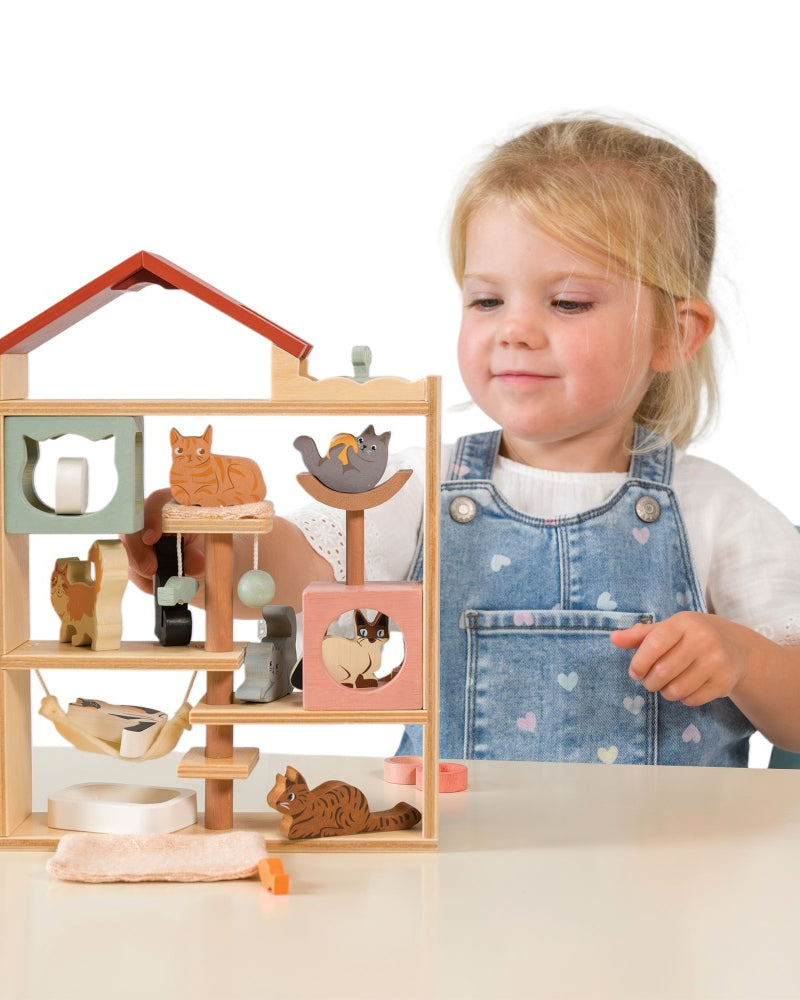 Child playing with a wooden toy house featuring animal figures on a white background
