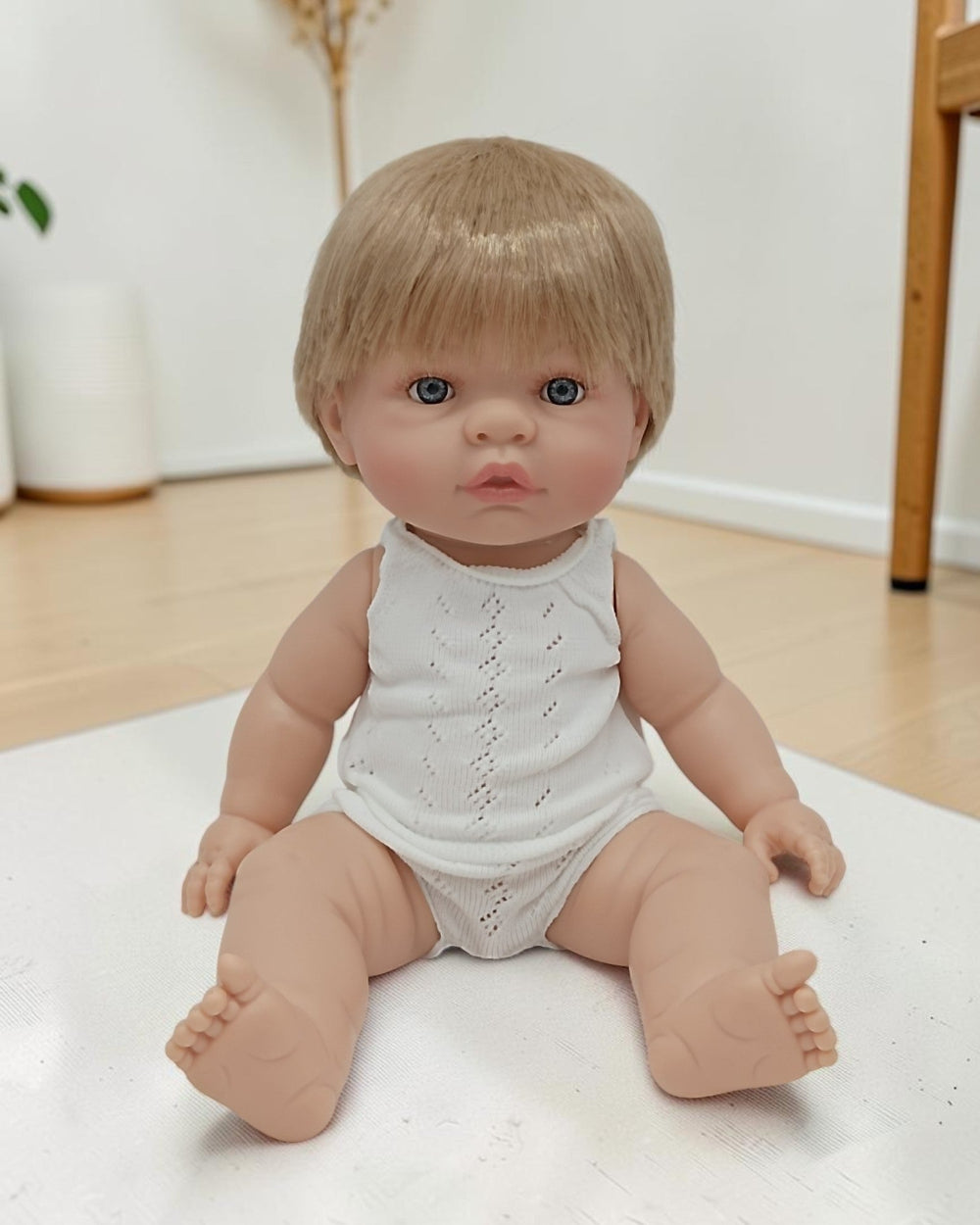 Realistic baby doll with blonde hair and blue eyes wearing a white outfit on a light surface.