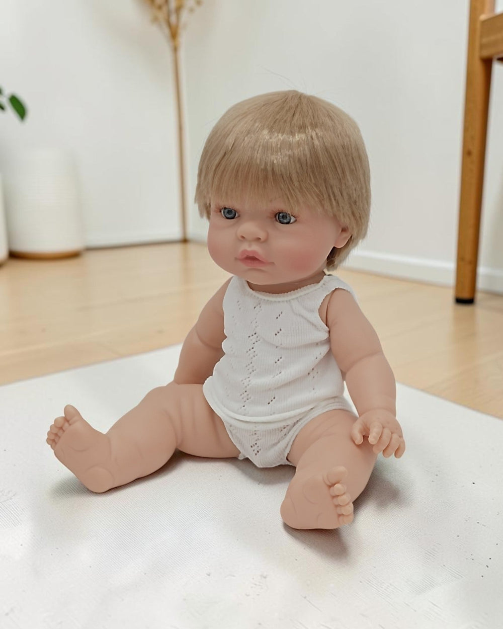 Baby doll with blonde hair and blue eyes sitting on a white surface.