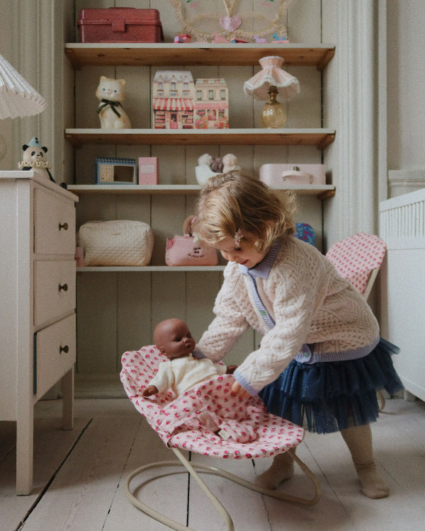 Child gently placing doll in rose bouncer during nurturing pretend play, developing empathy and care skills