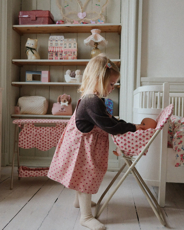 Child feeding doll in rose high chair during nurturing pretend play, demonstrating realistic mealtime scenarios