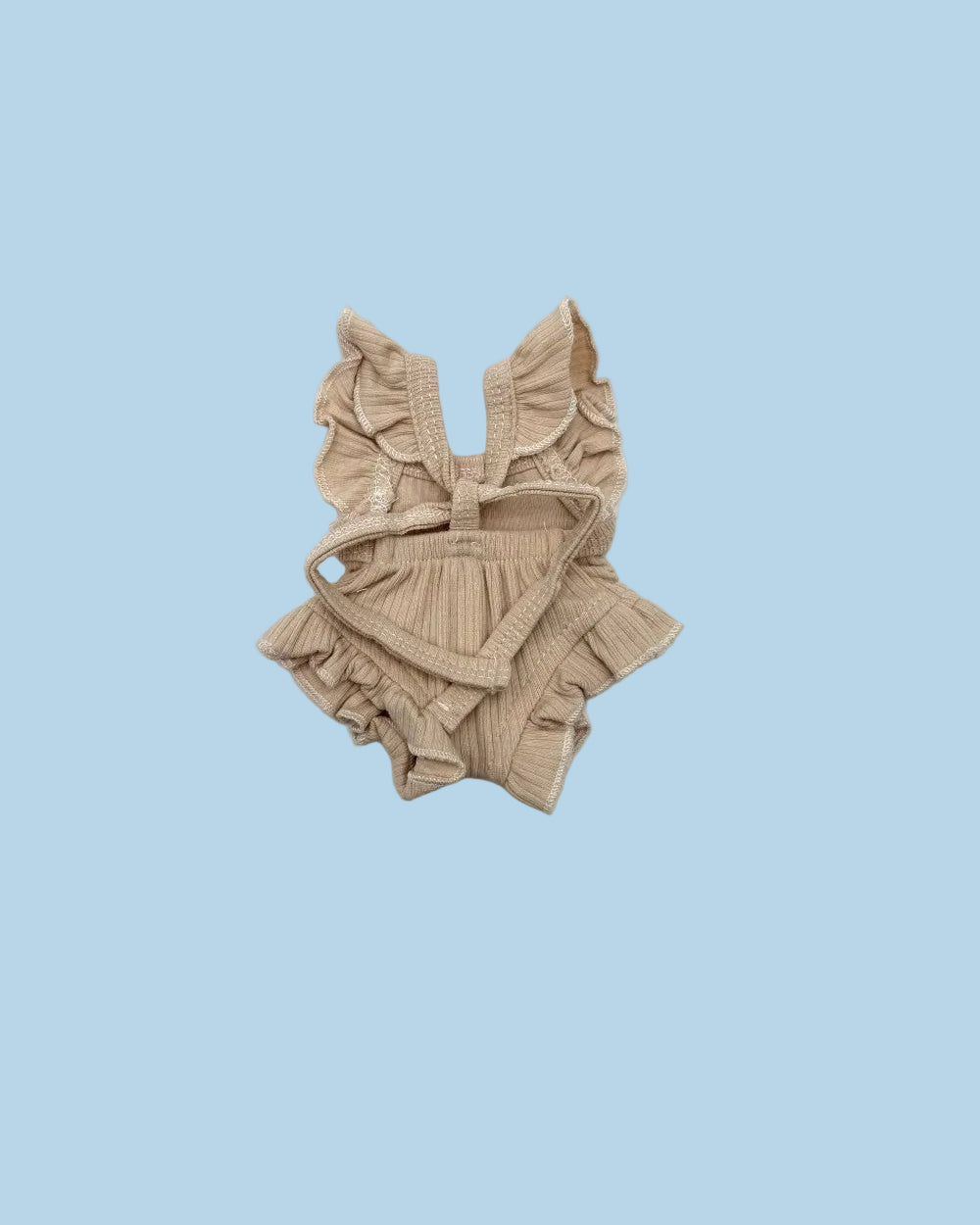 A beige ribbed knit baby romper with ruffled shoulder straps, a tie detail at the chest, and ruffled trim along the neckline and bottom, laid flat on a white background.