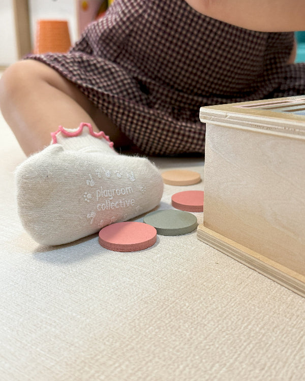 Toddler wearing grip socks while playing with dollhouse on hardwood floor