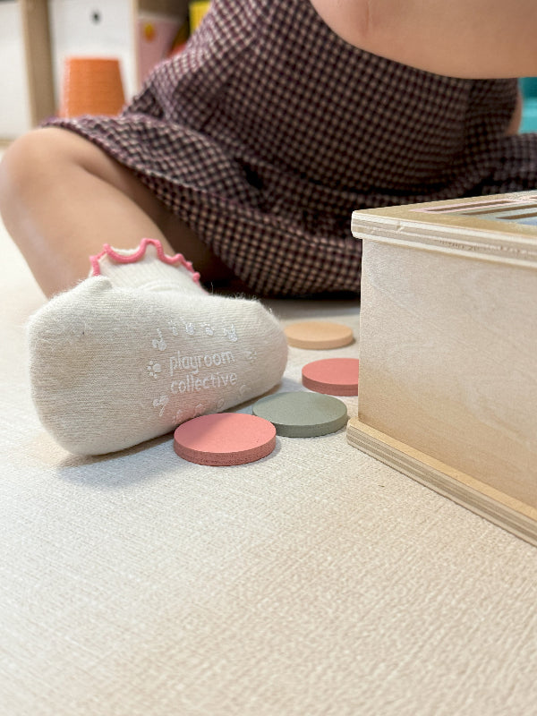 Toddler wearing grip socks while playing with dollhouse on hardwood floor