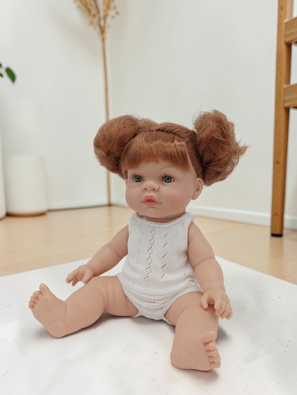 Realistic baby doll with red hair styled in buns sitting on a white surface.