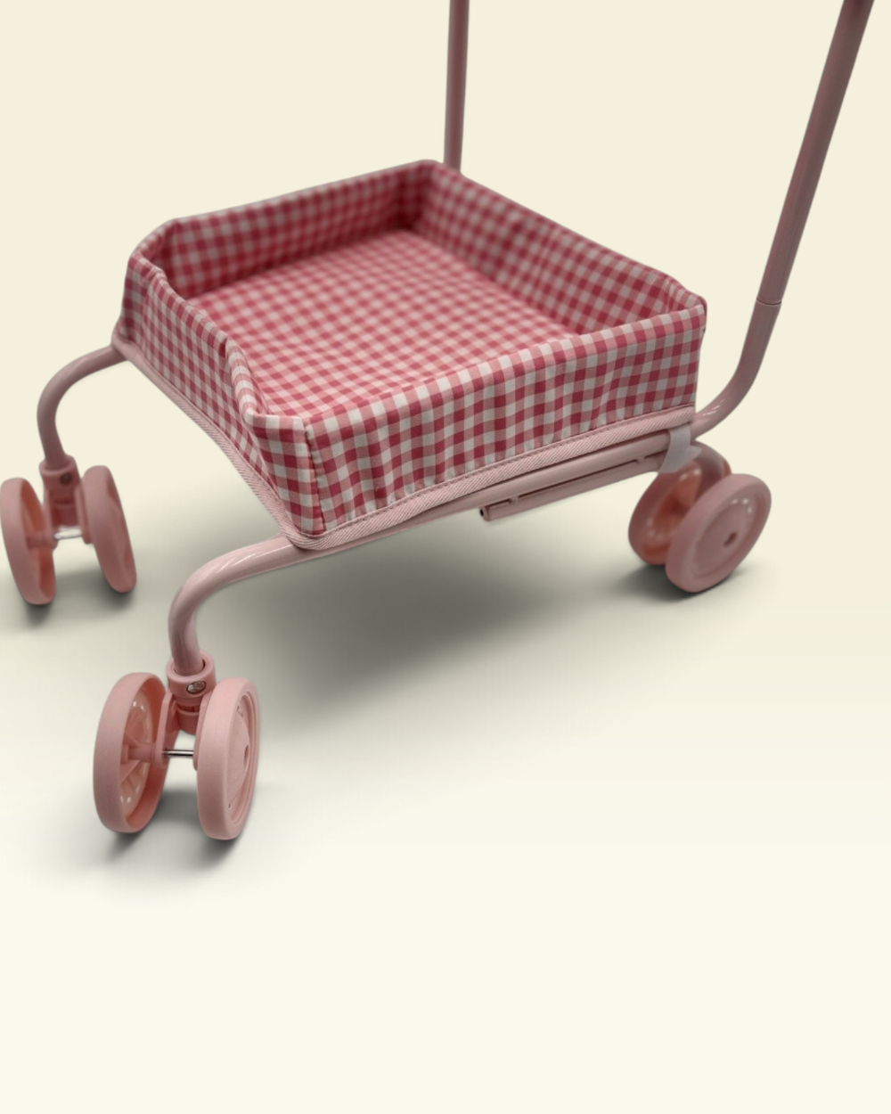 A pink toy shopping cart with a red and white gingham checkered cushion inside, shown on a plain light beige background.
