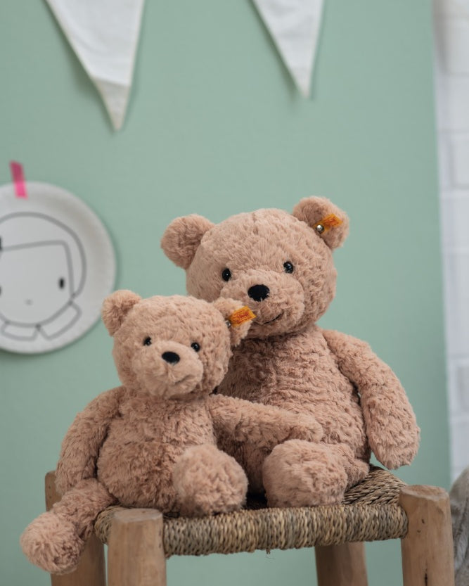 Two teddy bears sitting on a wooden stool against a light green wall.