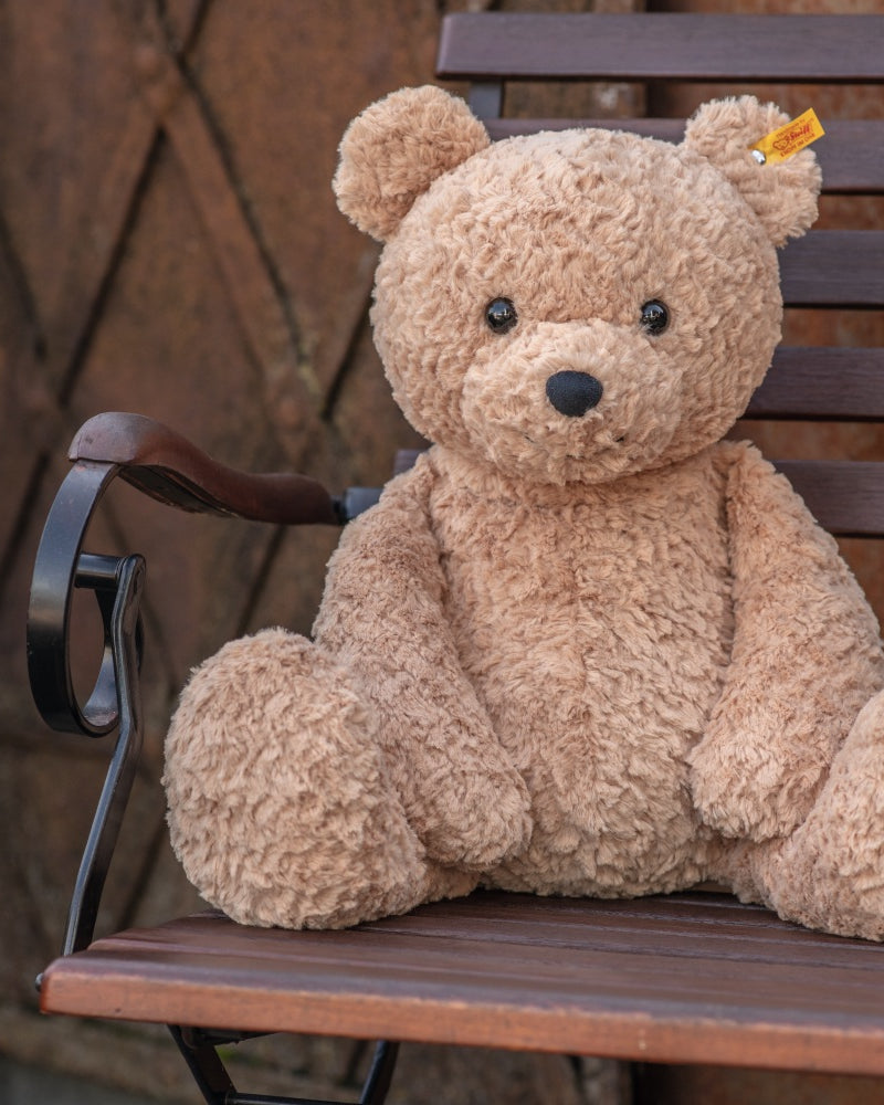 Brown teddy bear sitting on a wooden chair against a textured wall.