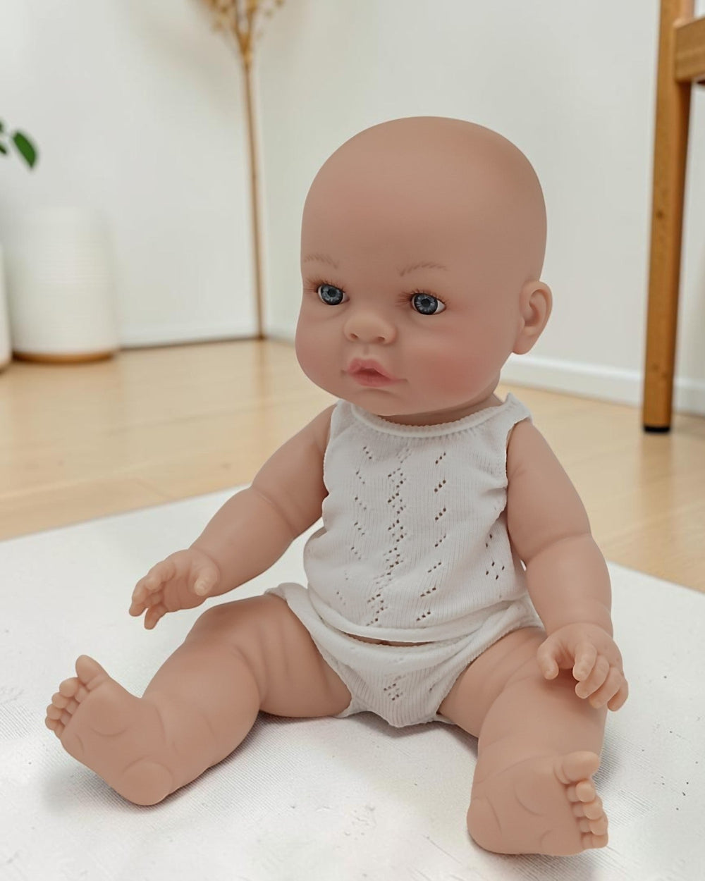 Baby doll wearing a white romper sitting on a light-colored surface.