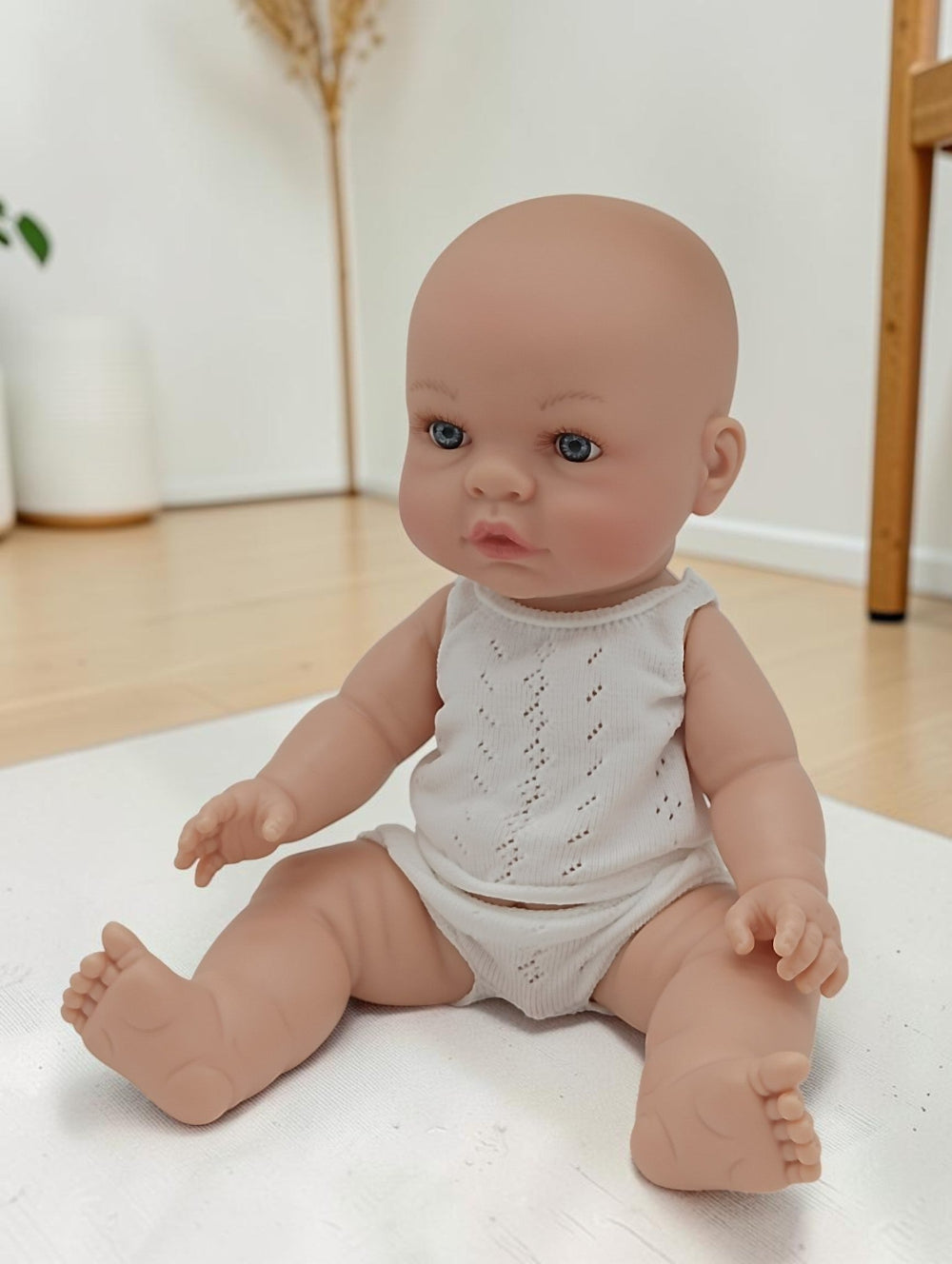 Baby doll wearing a white romper sitting on a light-colored surface.