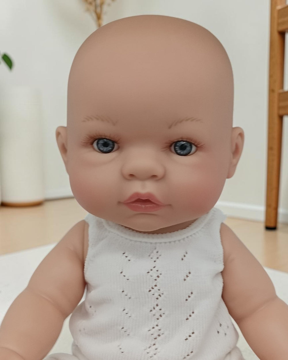 Realistic baby doll with blue eyes wearing a white outfit indoors.