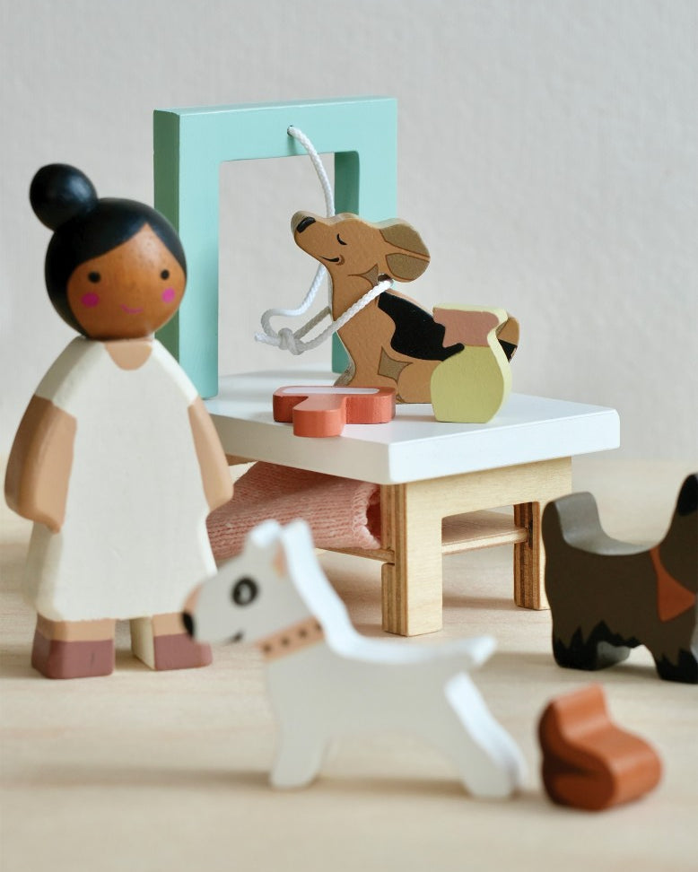Wooden toy figures of a girl and a dog with a small table and other toys on a light background