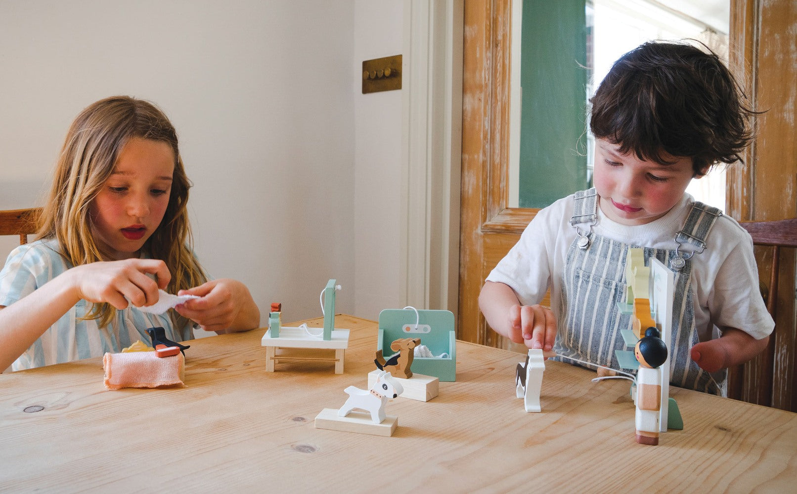 Two children playing with small figurines on a wooden table.