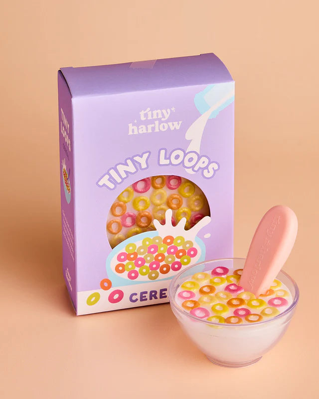Box of 'tiny harlow' Tiny Loops cereal with a bowl of cereal and pink spoon on a beige background