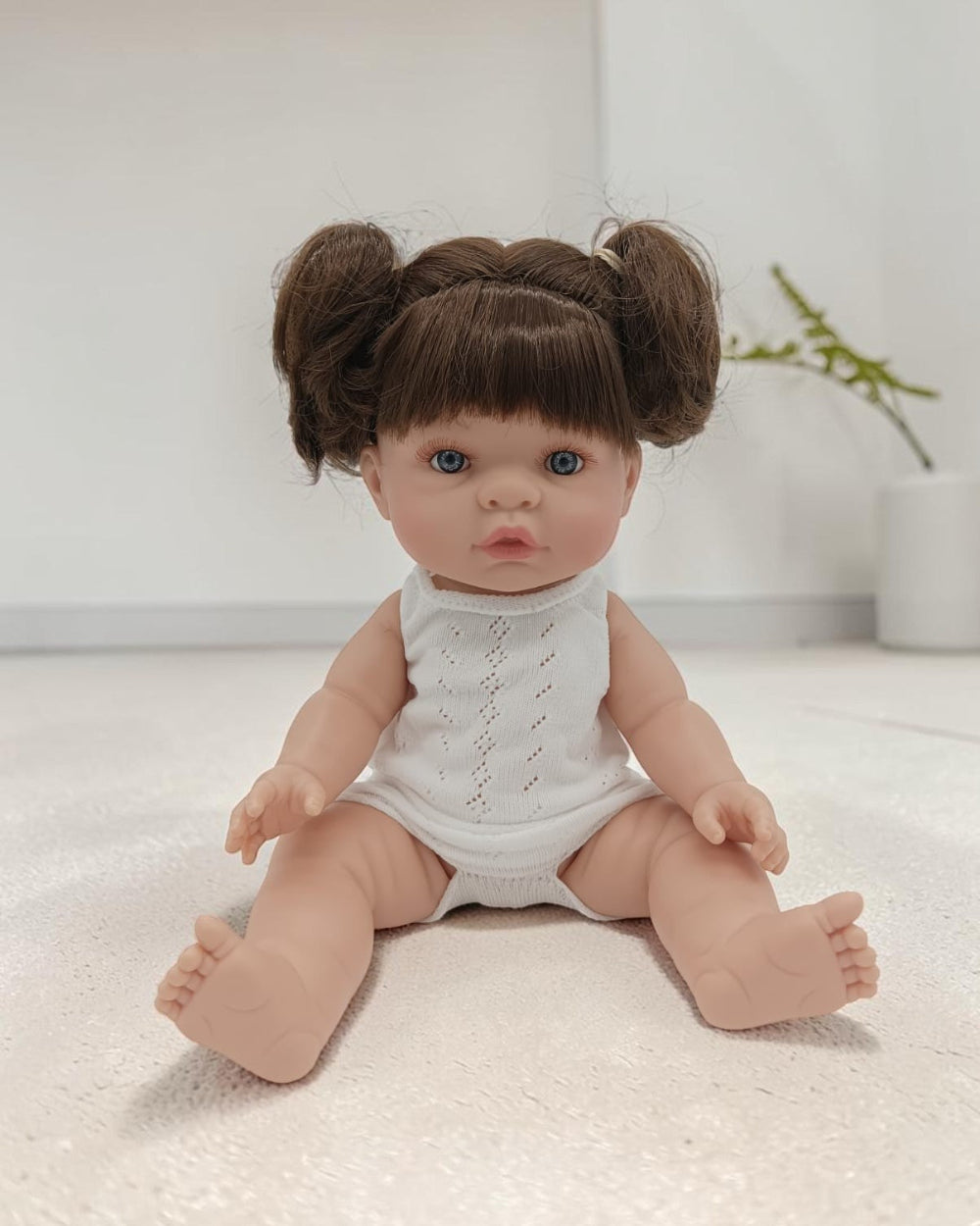 Baby doll with brown hair styled in buns wearing a white outfit on a light surface.