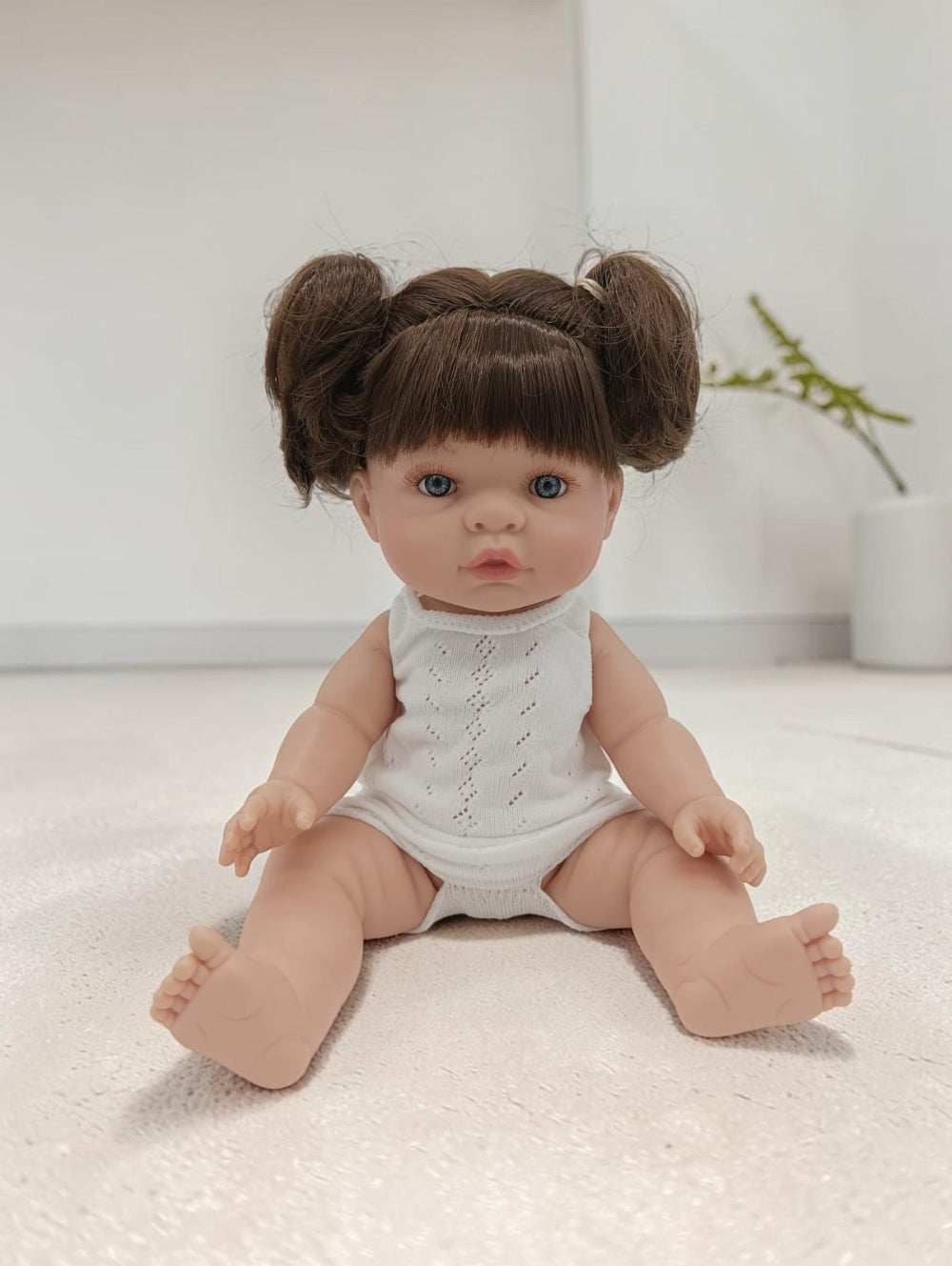 Baby doll with brown hair styled in buns wearing a white outfit on a light surface.