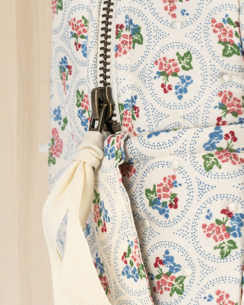 Close-up of bronze zipper with cream ribbon pull on floral patterned children's doll bag