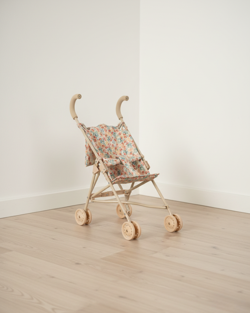 Small wooden toy stroller with floral canopy on a light wooden floor against a white wall.