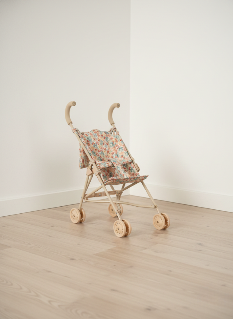 Small wooden toy stroller with floral canopy on a light wooden floor against a white wall.