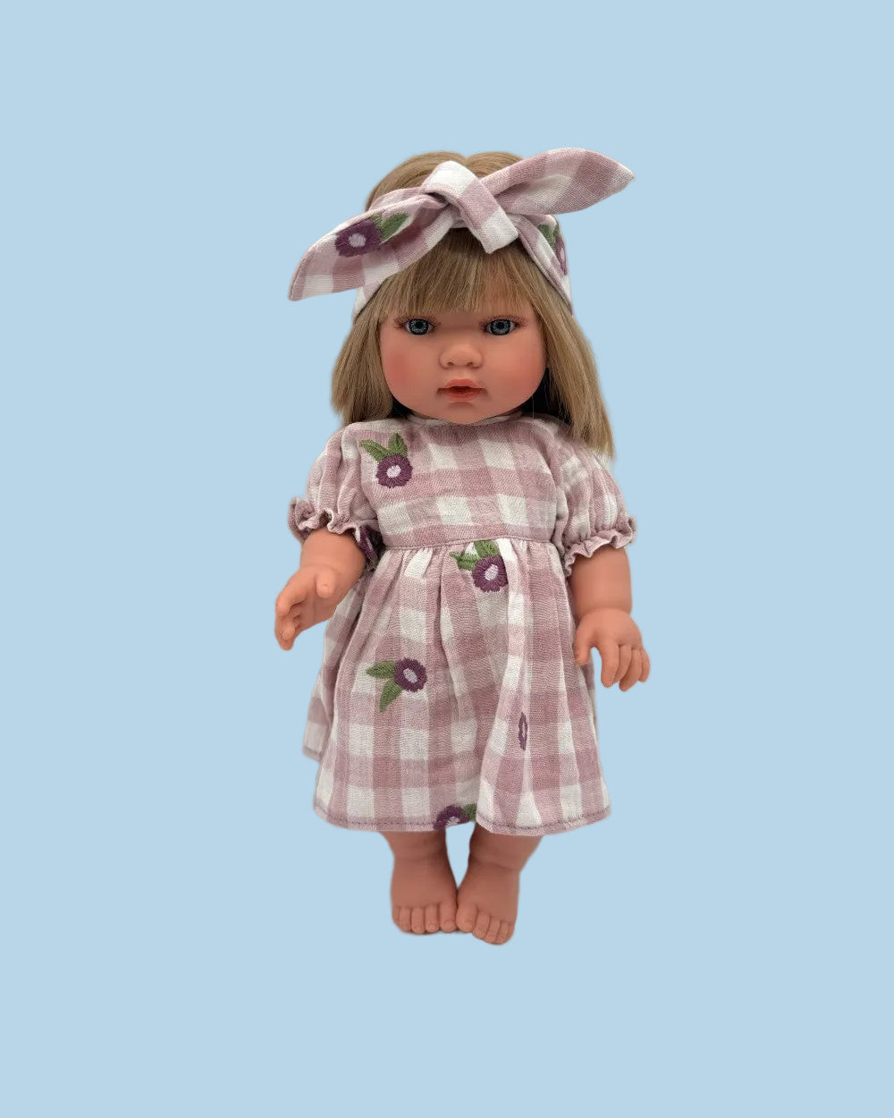 A doll with blonde hair wearing a purple and white gingham dress with flower motifs and a matching bow headband