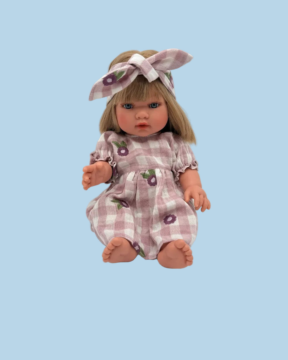 A porcelain doll with blonde hair, blue eyes, and a pink and white gingham outfit with purple flower prints, sitting against a light gray background.