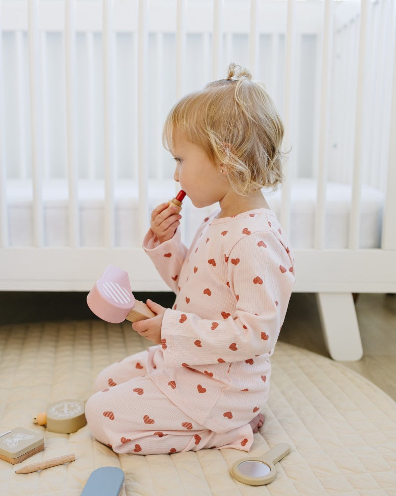 Child in a heart-patterned outfit sitting on the floor with toys around