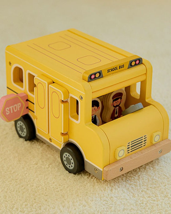 Close-up of wooden student and driver figures with warm hand-painted illustrations standing beside yellow school bus