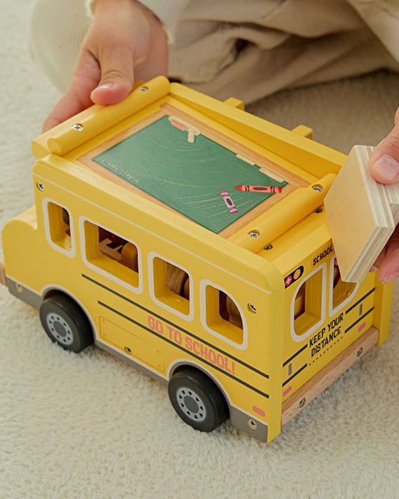 Child's hand pushing wooden school bus with character figure seated in driver's seat behind steering wheel