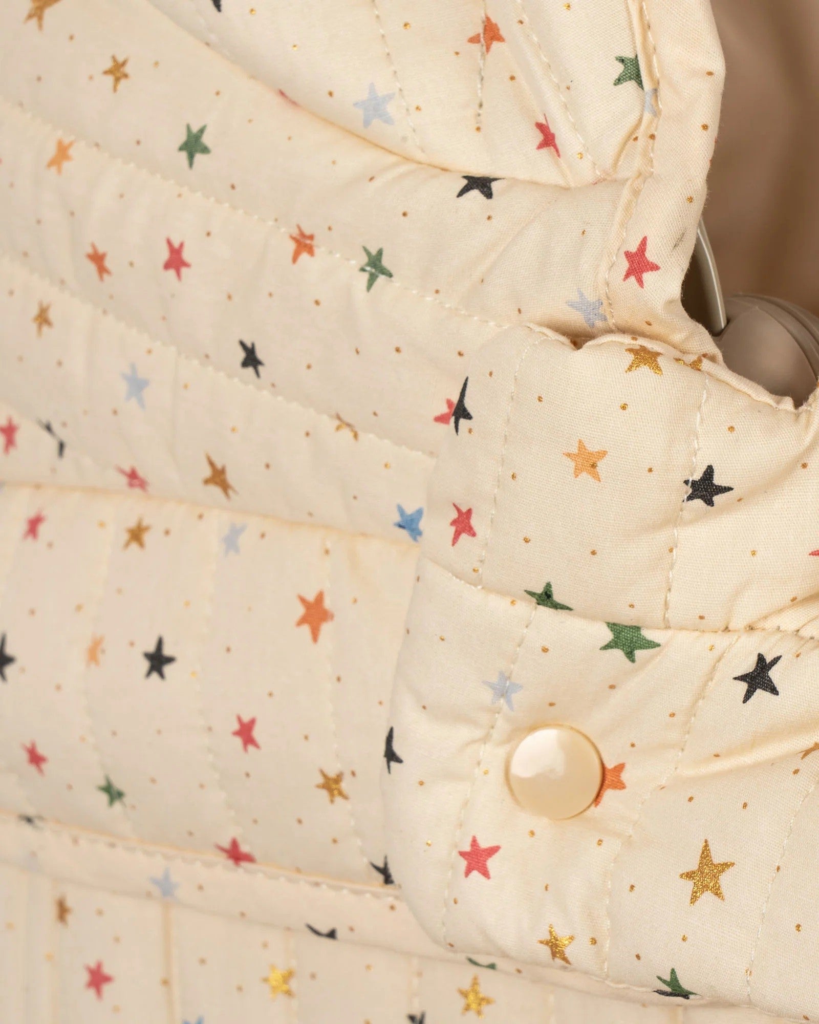 Charming cream and star pattern doll pram with four spoked wheels and quilted fabric details