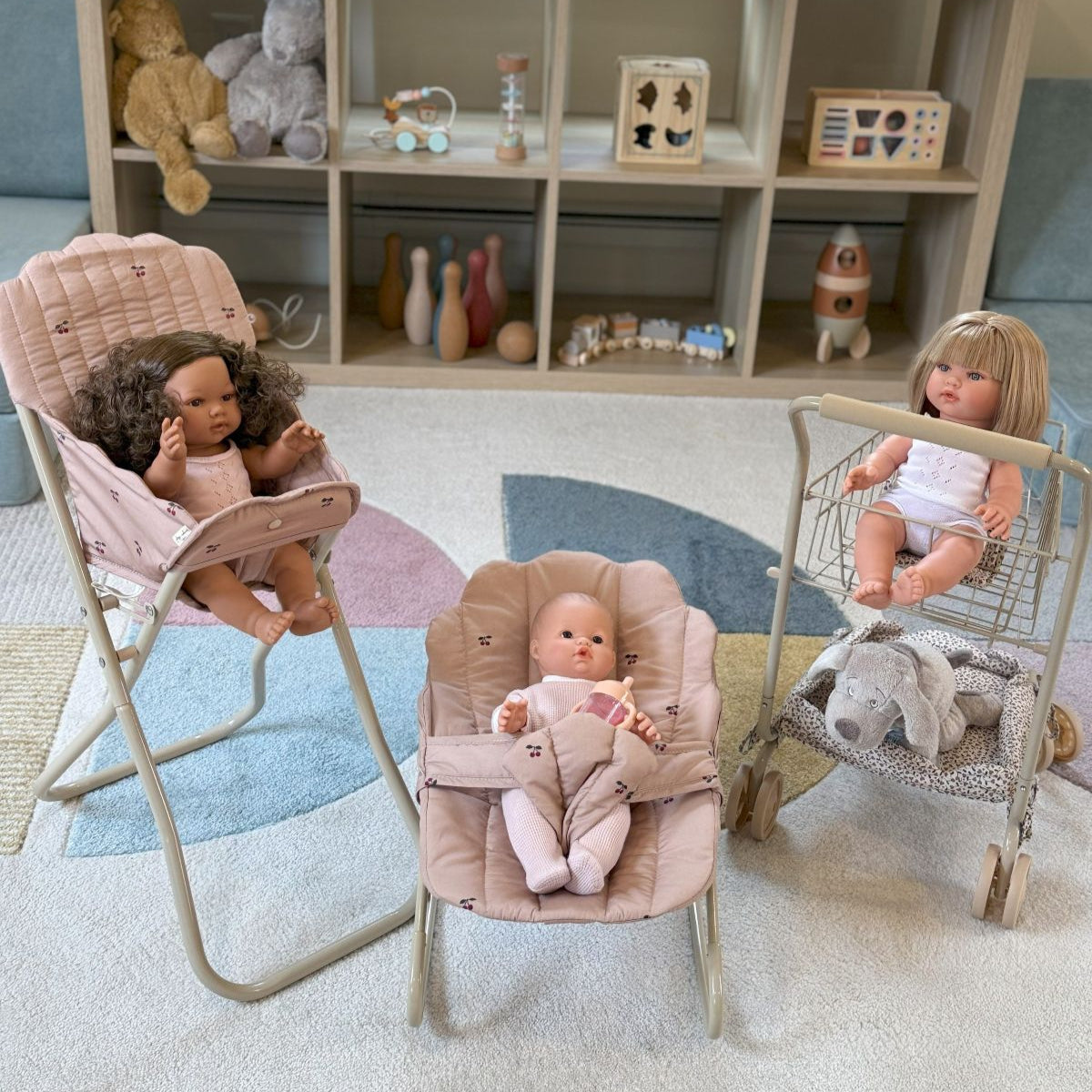 Three dolls in a playroom setting with toys and furniture.