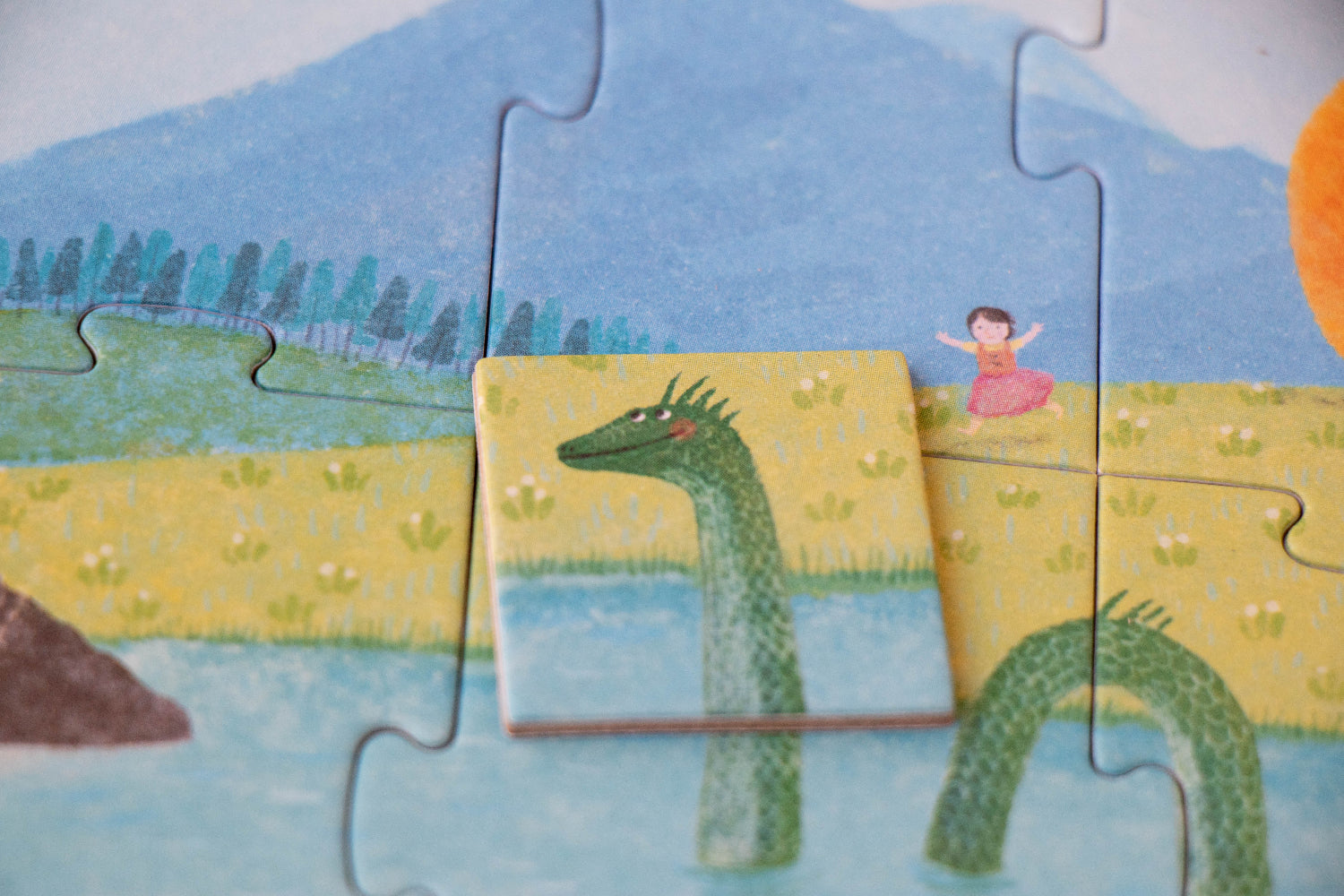 Children's puzzle with a dragon and a girl on a yellow platform, set against a scenic background.