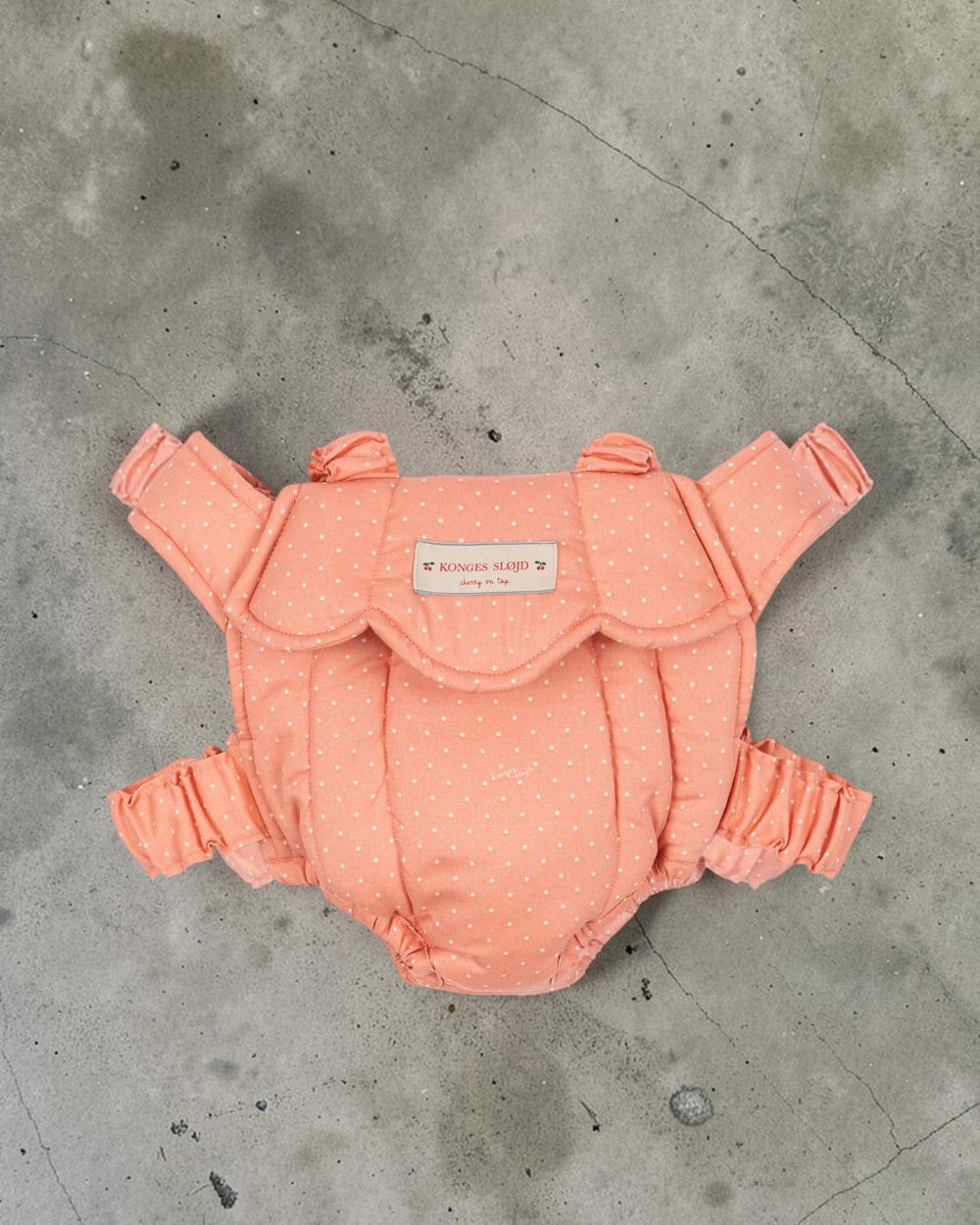 Playroom Collective Konges Sloejd baby doll carrier in coral pink with white dots and scalloped edge detail.