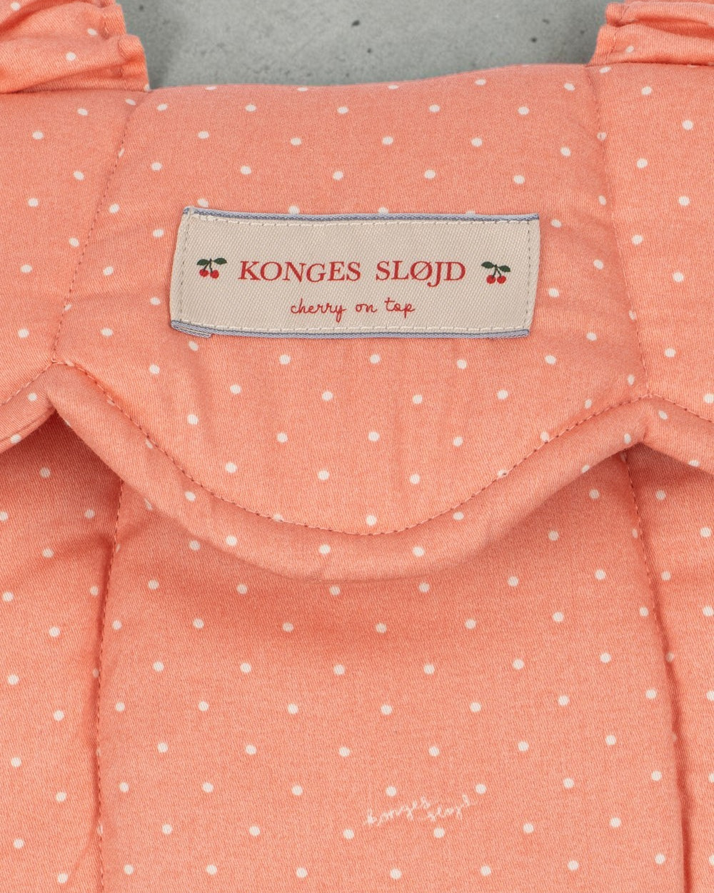 Playroom Collective Konges Sloejd baby doll carrier in coral rose dot cotton with a scalloped edge and brand label.