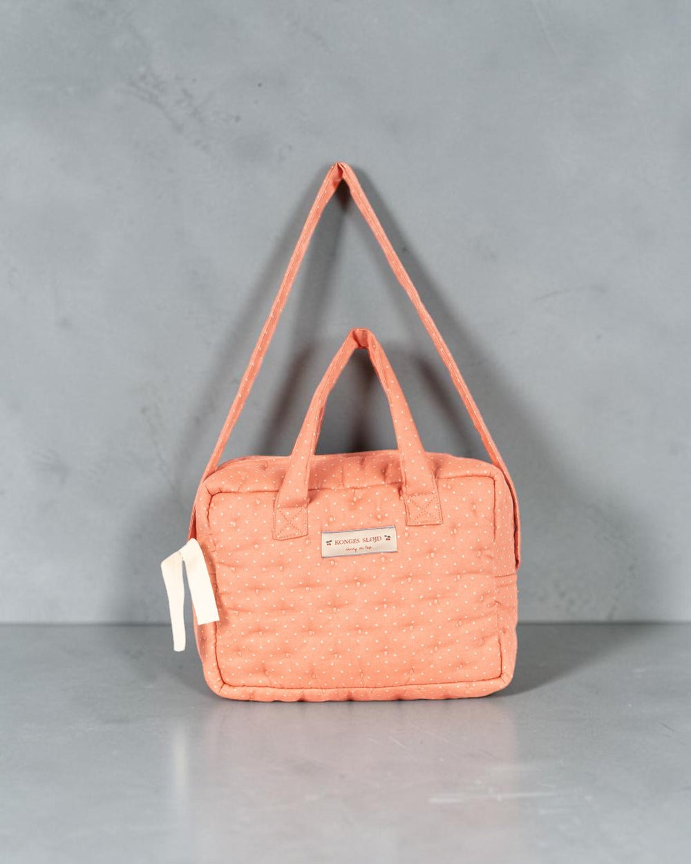 Playroom Collective Konges Sloejd doll diaper bag in coral cotton with white dot pattern and adjustable strap.