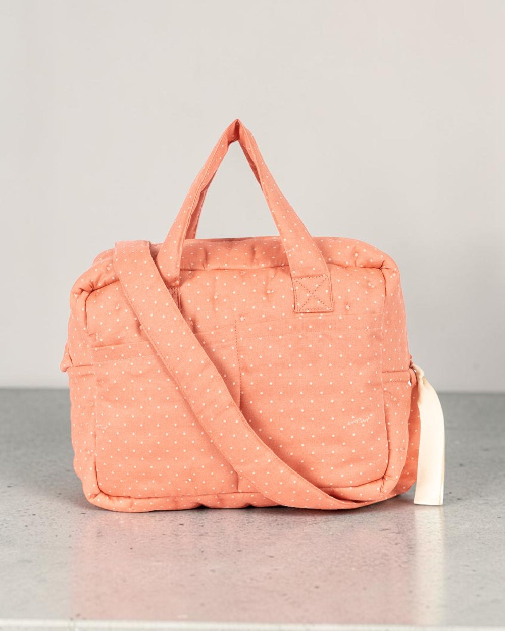 Playroom Collective Konges Sloejd doll diaper bag in coral cotton with white dots, featuring handles and strap.