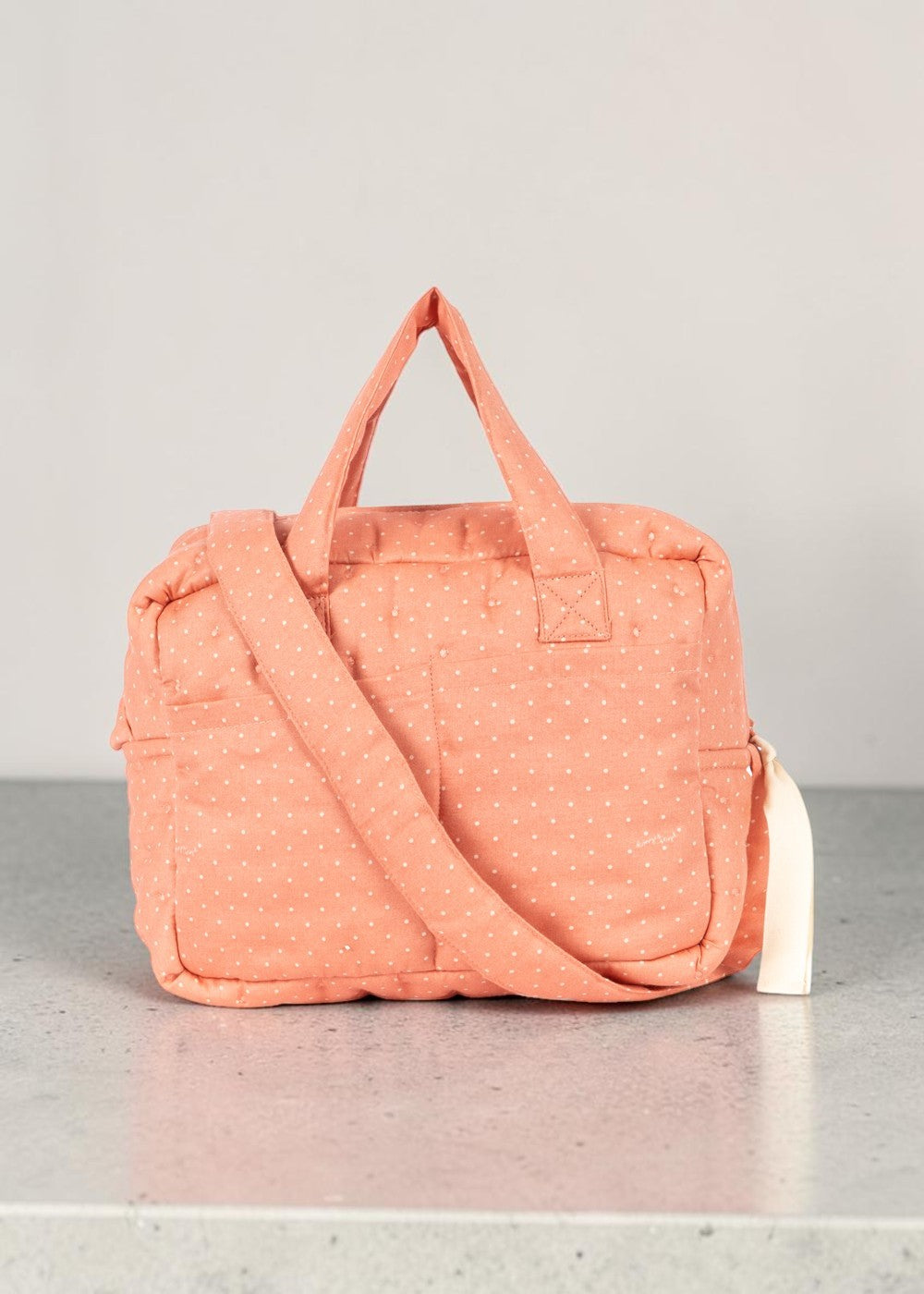 Playroom Collective Konges Sloejd doll diaper bag in coral cotton with white dots, featuring handles and strap.