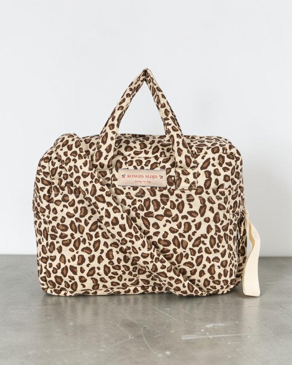 Playroom Collective Konges Sloejd leopard print cotton doll diaper bag with top handles and crossbody strap.