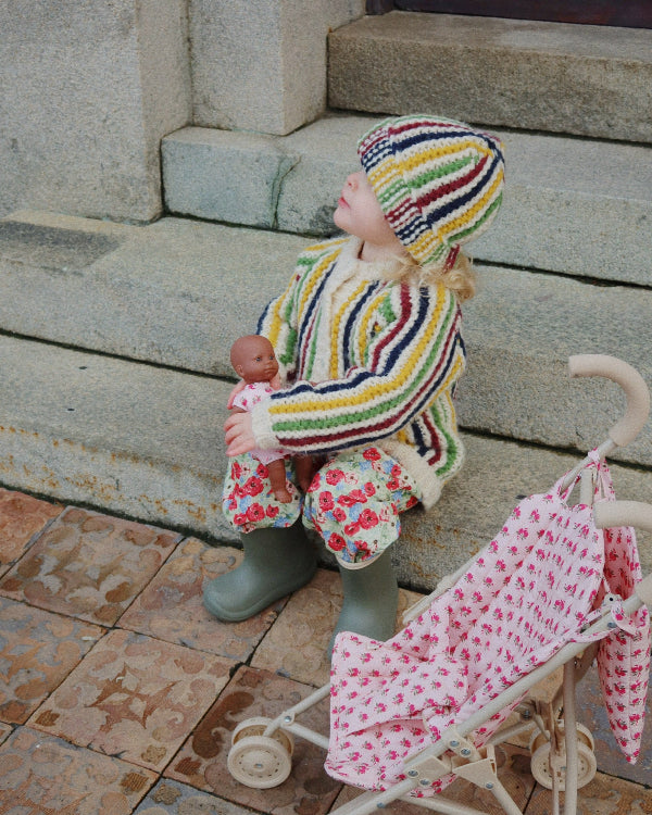 Child in a colorful knitted outfit with a baby and a stroller on a stone step.