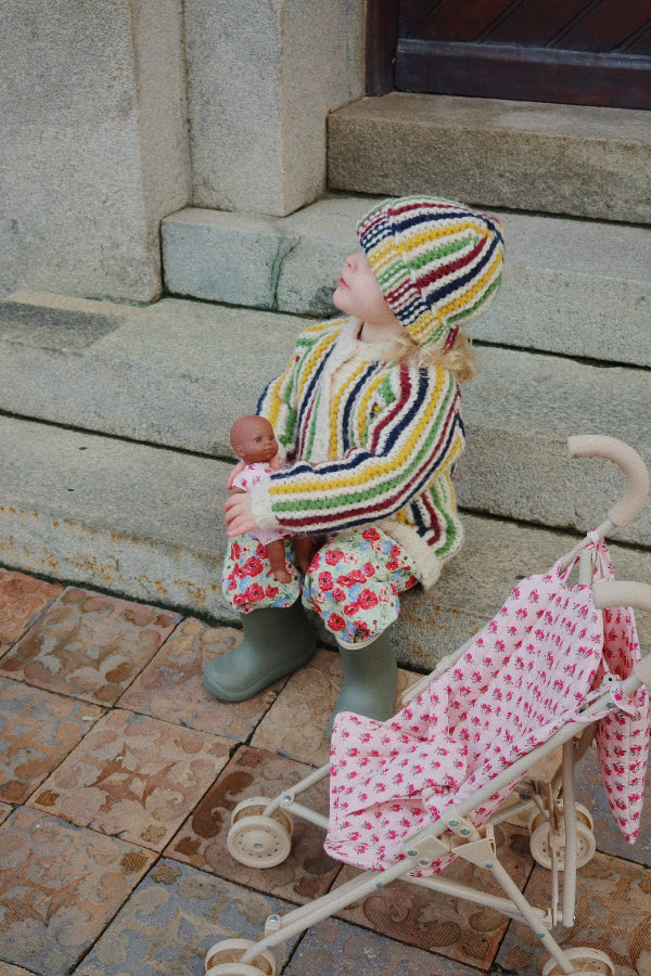 Child in a colorful knitted outfit with a baby and a stroller on a stone step.